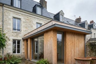 Extension en bois moderne accolée à une maison de ville nantaise, vue depuis le jardin avec contraste entre pierre ancienne et bardage en douglas naturel